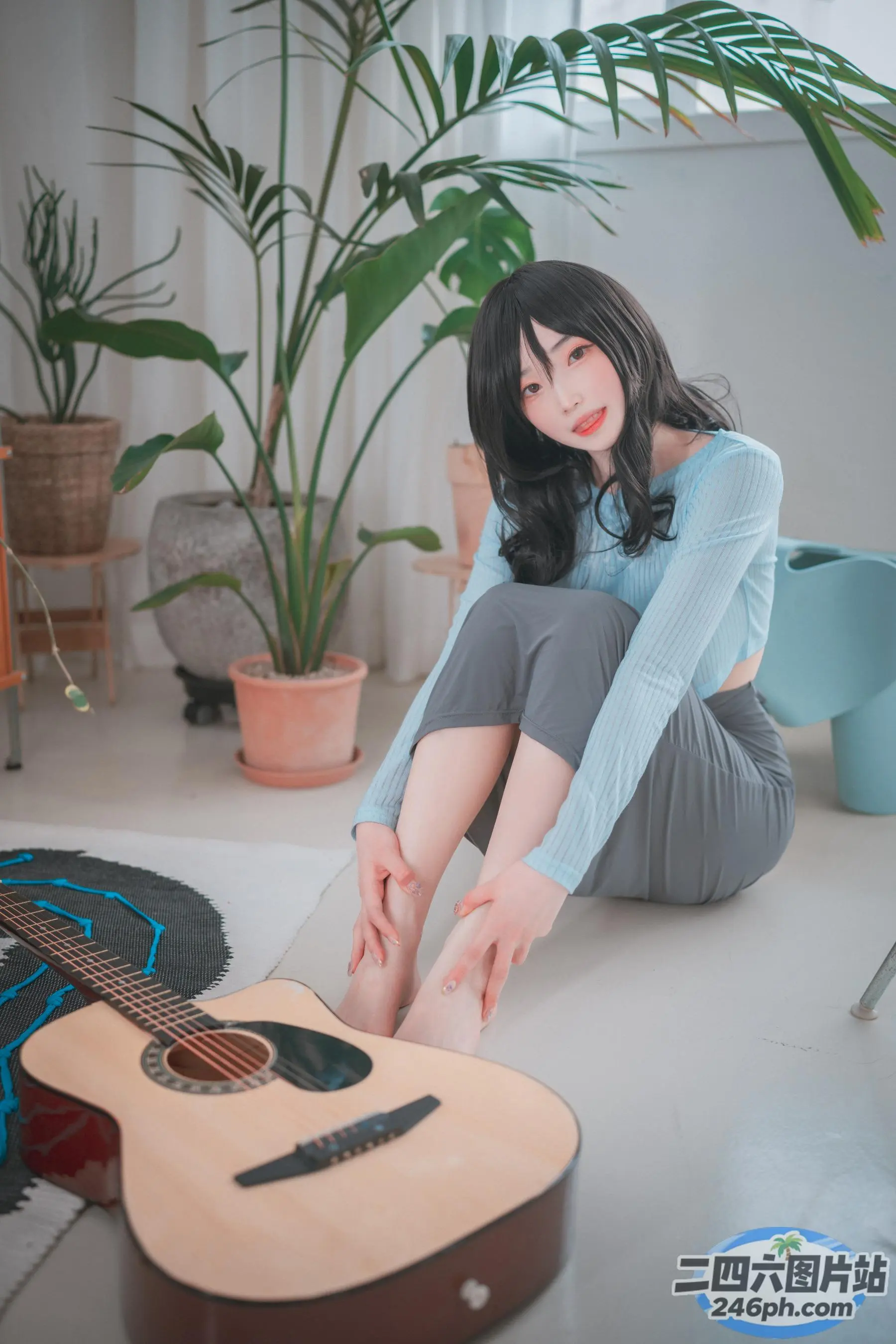 女人坐在地板上，手里拿着吉他和一棵植物