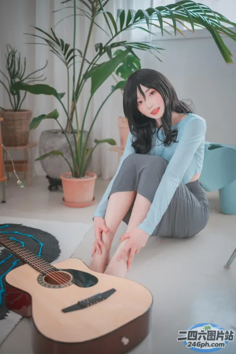 女人坐在地板上，手里拿着吉他和一棵植物