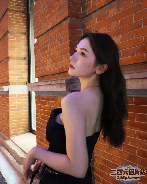 身穿黑色连衣裙的 araffe 女子站在一座砖砌建筑前