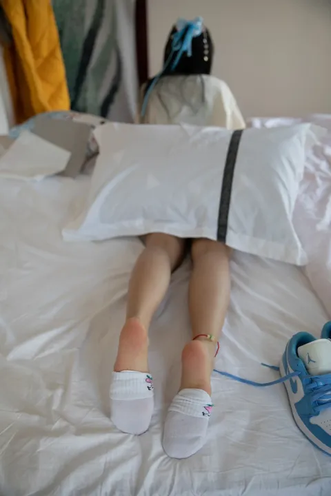 有人躺在床上，双脚抬起，手里拿着一双鞋