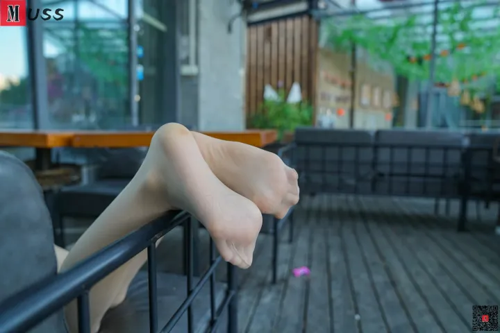 有一个人坐在长凳上，脚踩在栏杆上