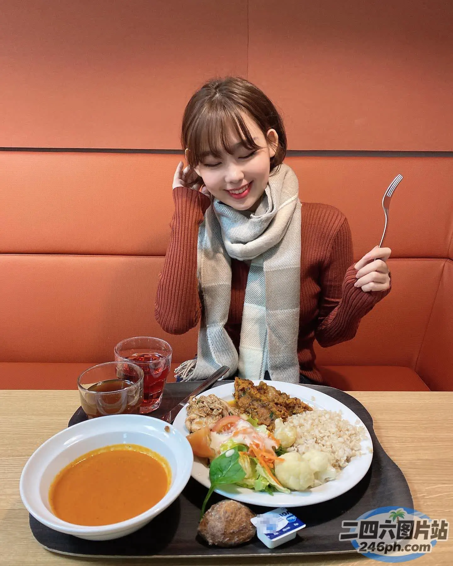 女人坐在桌子旁，手里拿着一盘食物和一碗汤