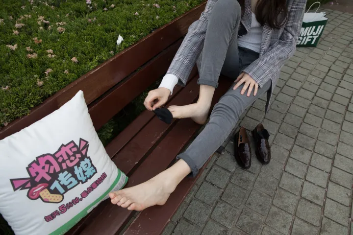 女人坐在长凳上，双脚撑在枕头上