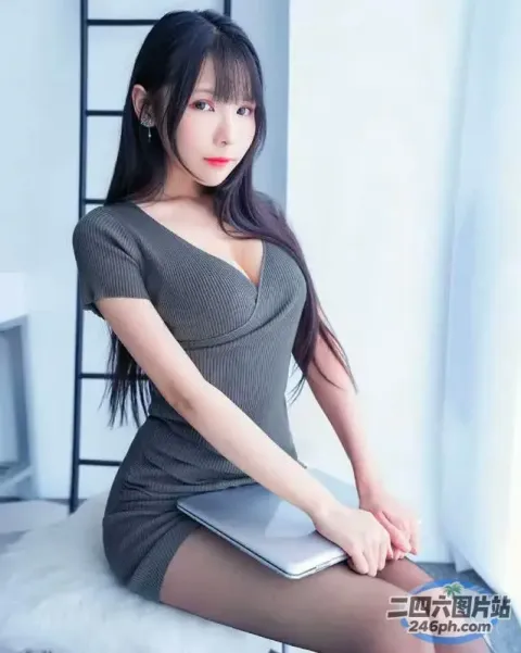 一个穿着灰色连衣裙的女人坐在床上，手里拿着一台笔记本电脑