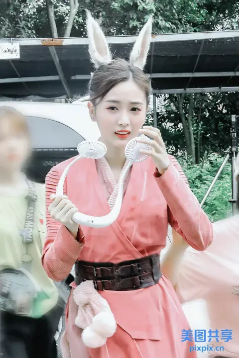 有一个穿着粉色连衣裙的女人，手里拿着一条白蛇