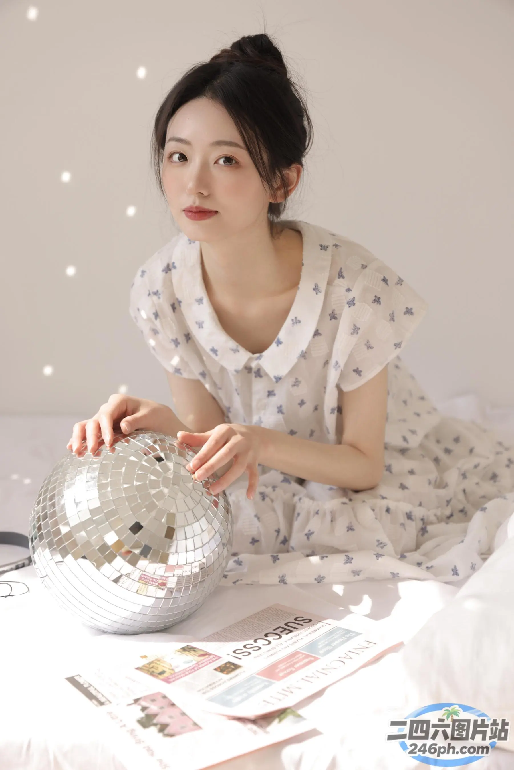 有一个女人坐在一张床上，手里拿着一个迪斯科球