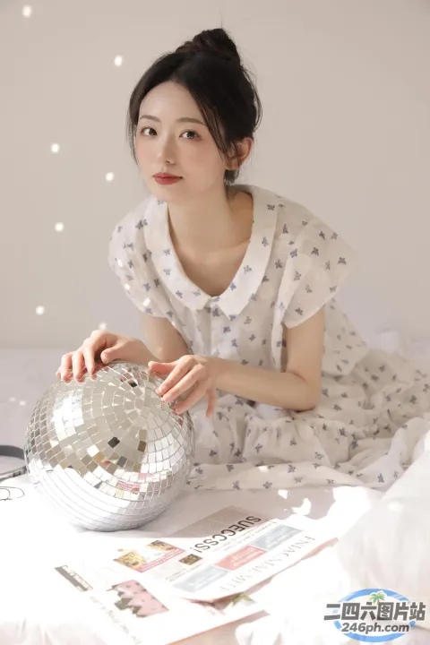 有一个女人坐在一张床上，手里拿着一个迪斯科球