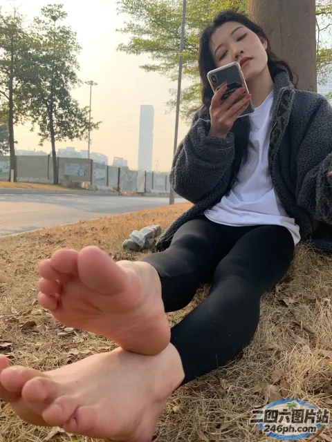阿拉菲坐在地上，双脚抬起，手里拿着手机