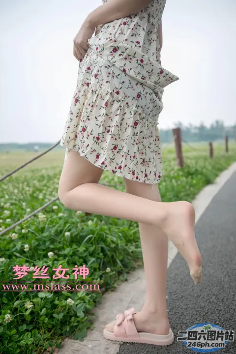一名穿着连衣裙的女人双腿交叉站在人行道上