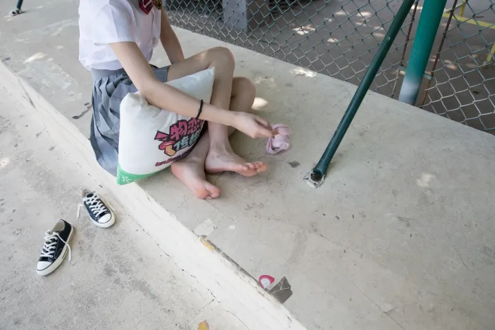 有一个小男孩坐在路边，双脚撑着