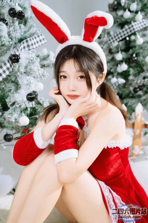 阿拉菲身着红白相间的衣服，坐在圣诞树旁