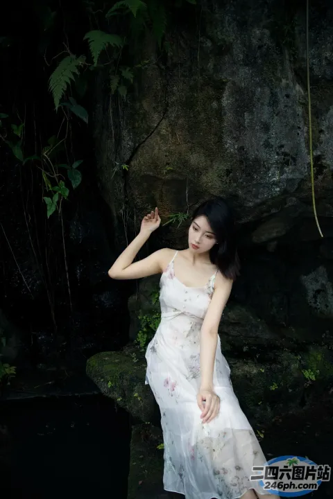 穿着白色连衣裙的 Arafed 女人坐在瀑布附近的岩石上