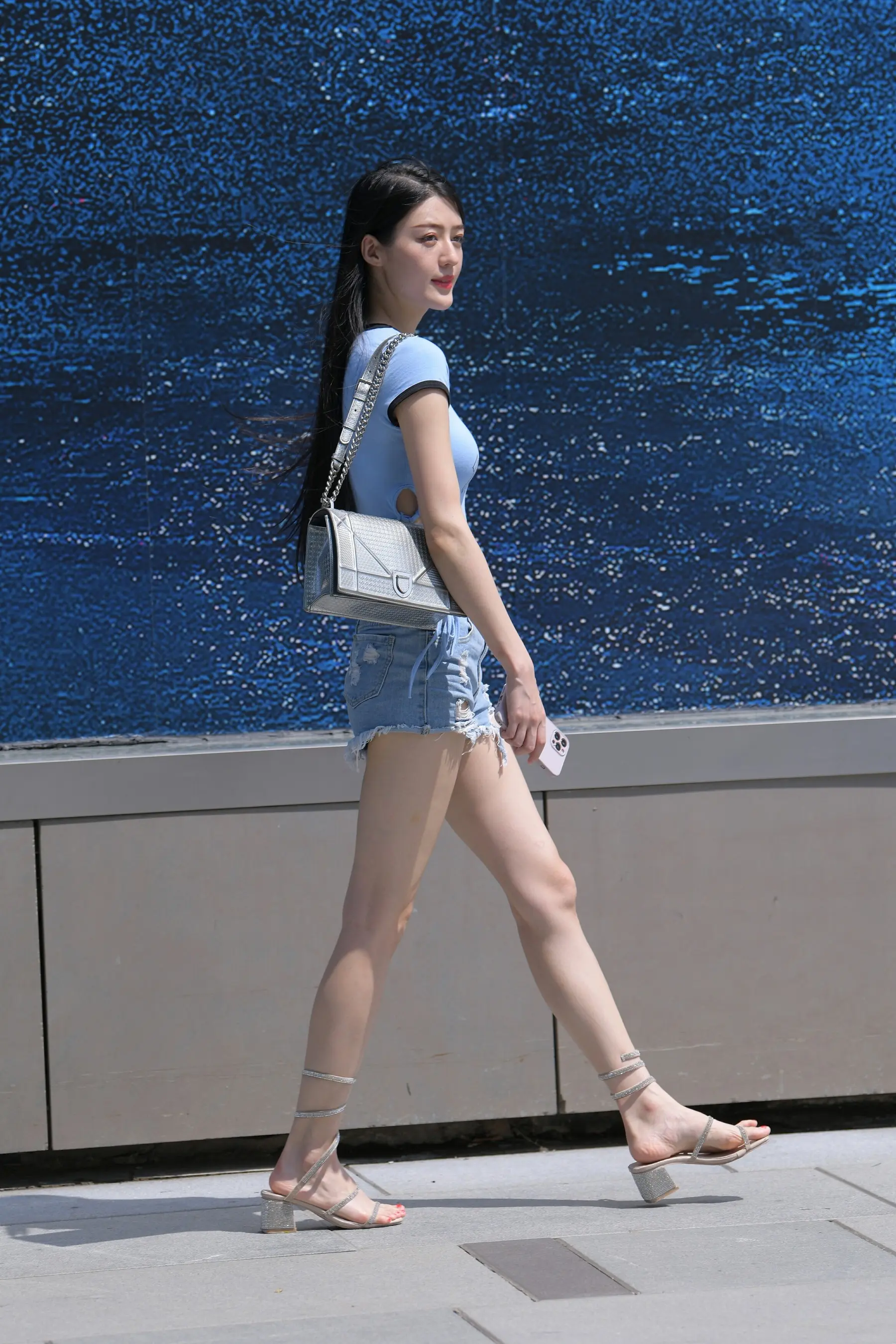 女人在人行道上走着，钱包和鞋子靠近墙