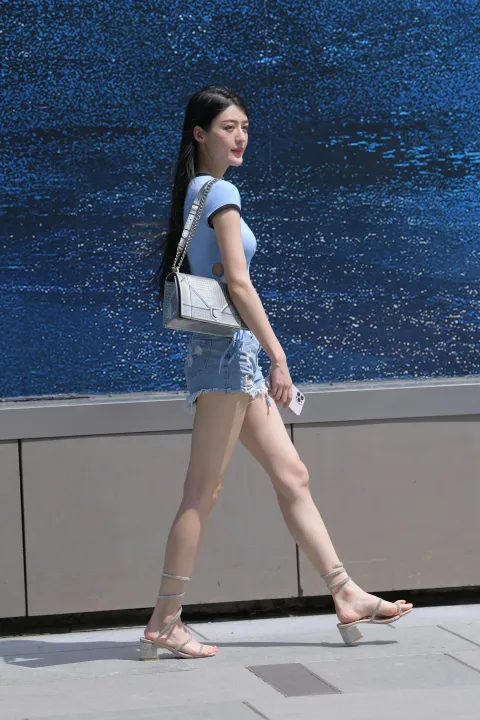 女人在人行道上走着，钱包和鞋子靠近墙
