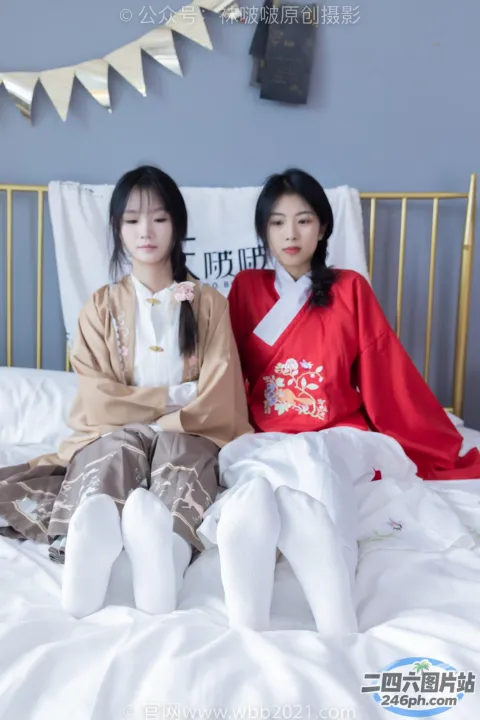两个女人坐在一个有白色床的房间里的一张床上