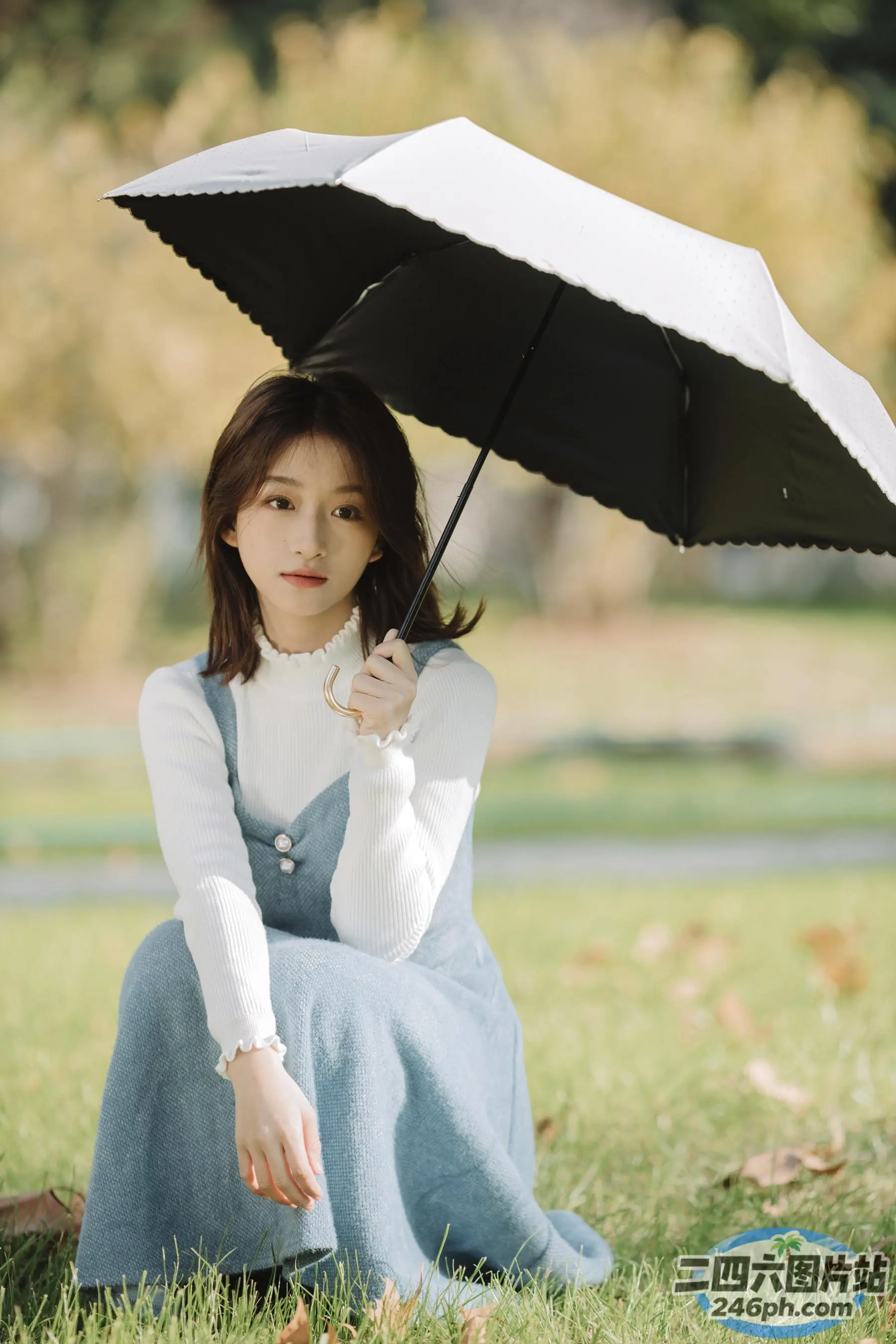 草地上坐着一个女人，手里撑着伞