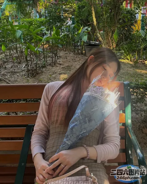 女人坐在长凳上，手里拿着一个袋子和一束鲜花