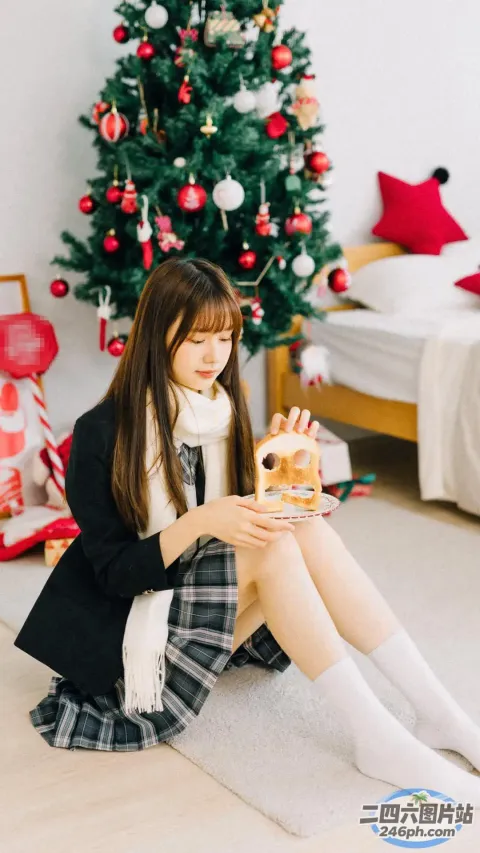 一个女人坐在地板上，手里拿着一盘食物，站在圣诞树前