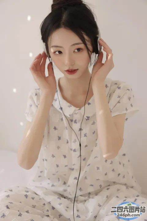 一个穿着白衬衫、戴着耳机的女人坐在床上