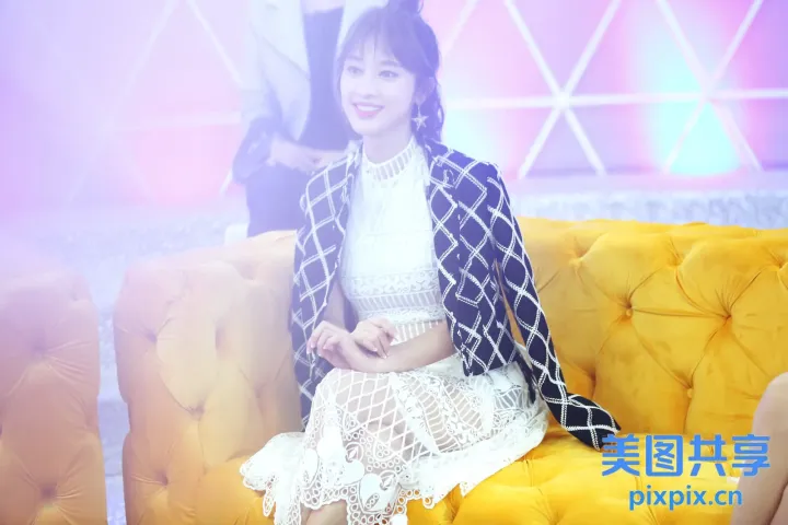 有一个女人坐在黄色的沙发上，穿着一件黑白夹克