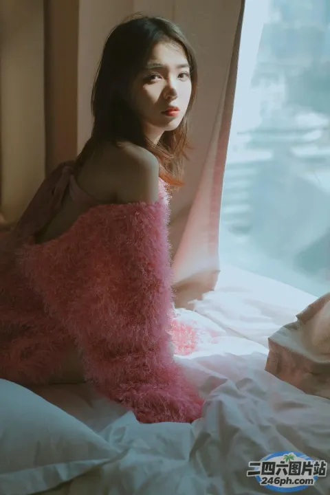 有一个女人坐在床上，上面盖着一条粉红色的毯子