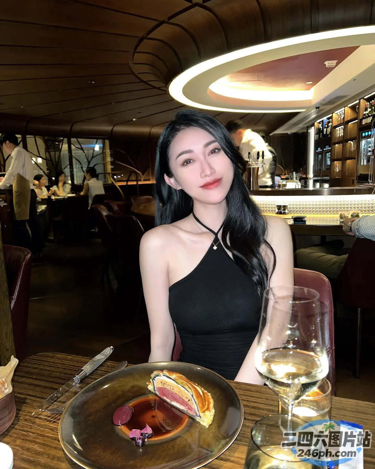 女人坐在桌子旁，手里拿着一盘食物和葡萄酒