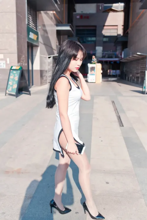 身穿白色连衣裙和黑色高跟鞋的 araffe 女子走在人行道上