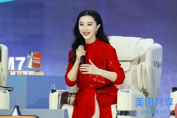 身穿红色连衣裙的女子手持麦克风，站在屏幕前