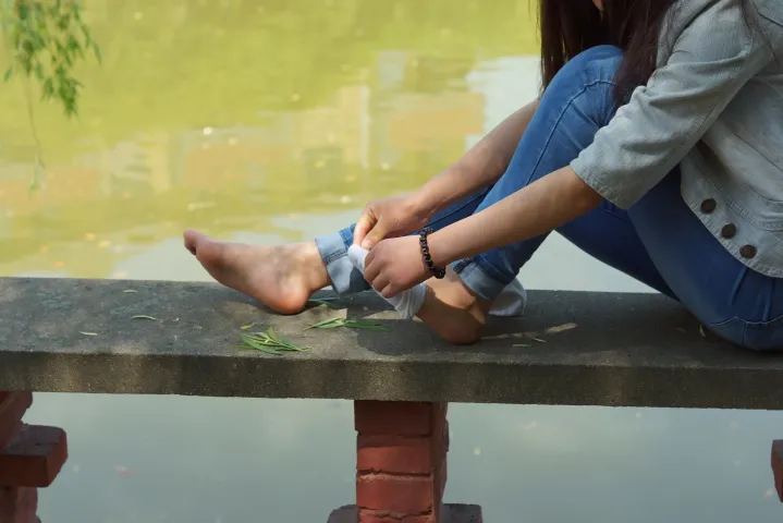有一个女人坐在长凳上，双脚踩在一张纸上
