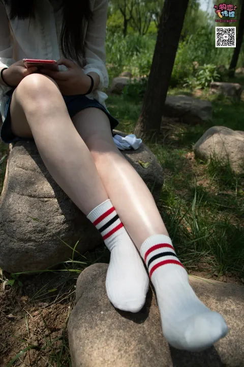 阿拉夫德女人坐在一块石头上，双腿交叉，手里拿着一部手机