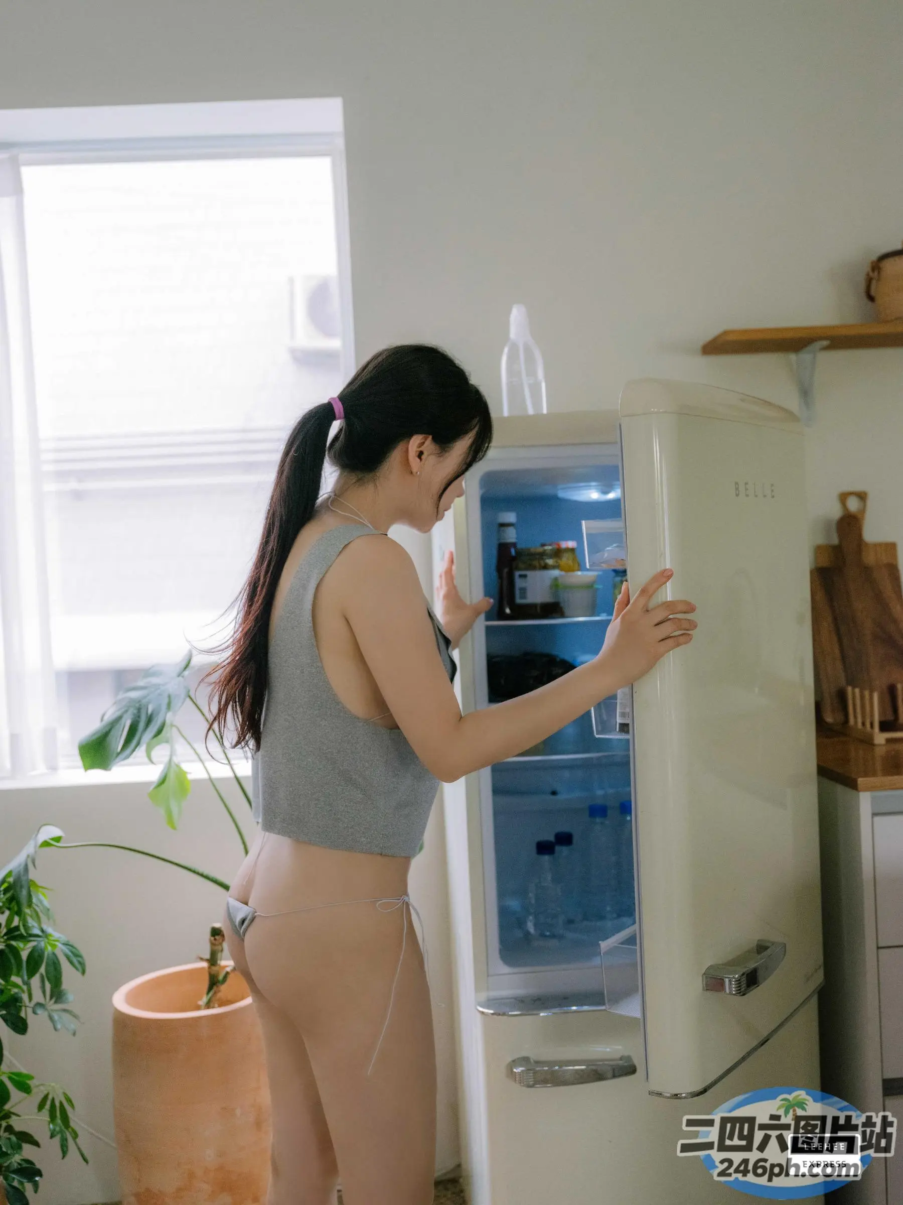 穿着灰色背心和裸色内裤的女人站在冰箱旁边的厨房里