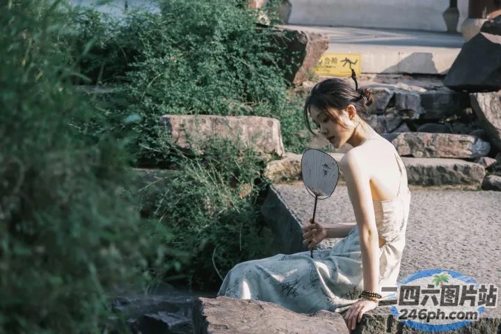 有个女人坐在石头上，手里拿着扇子