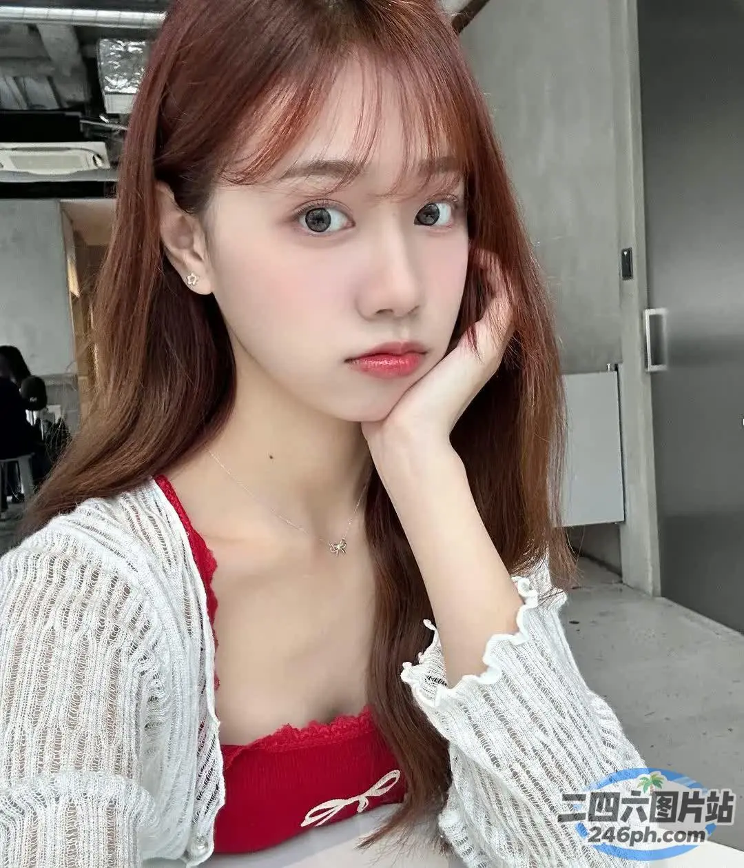 一位留着红色长发的女士坐在桌子旁，手里拿着一台笔记本电脑