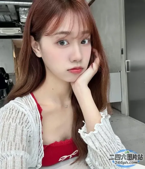 一位留着红色长发的女士坐在桌子旁，手里拿着一台笔记本电脑
