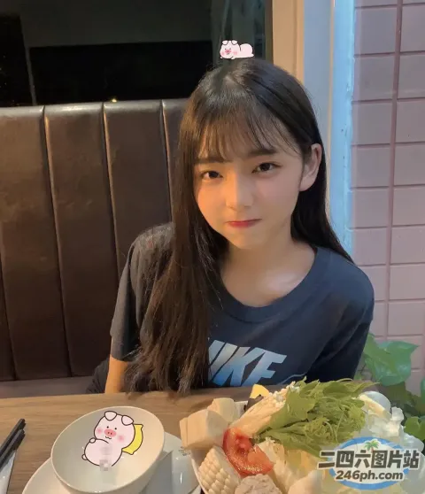 有个年轻女孩坐在一张桌子旁，桌上端着一盘食物