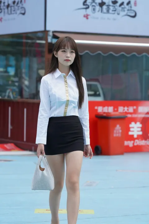 一个穿着裙子和白衬衫的女人走在街上