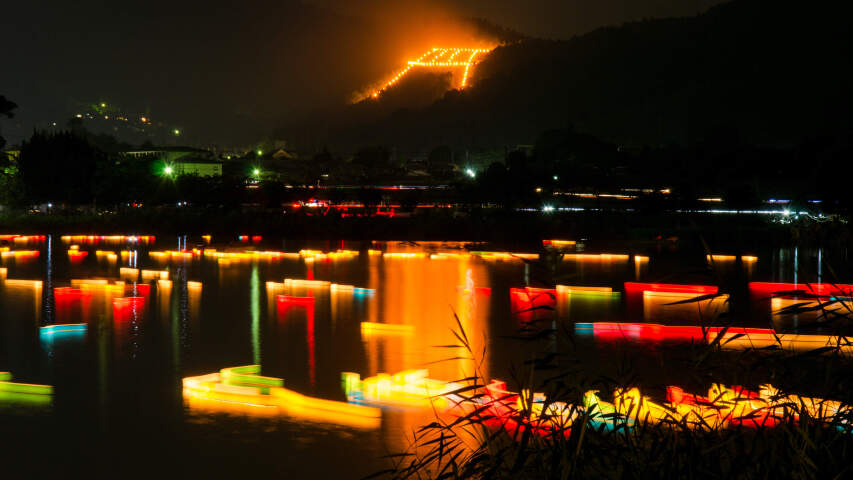 夜晚灯火通明的湖中船只，背景是一座山