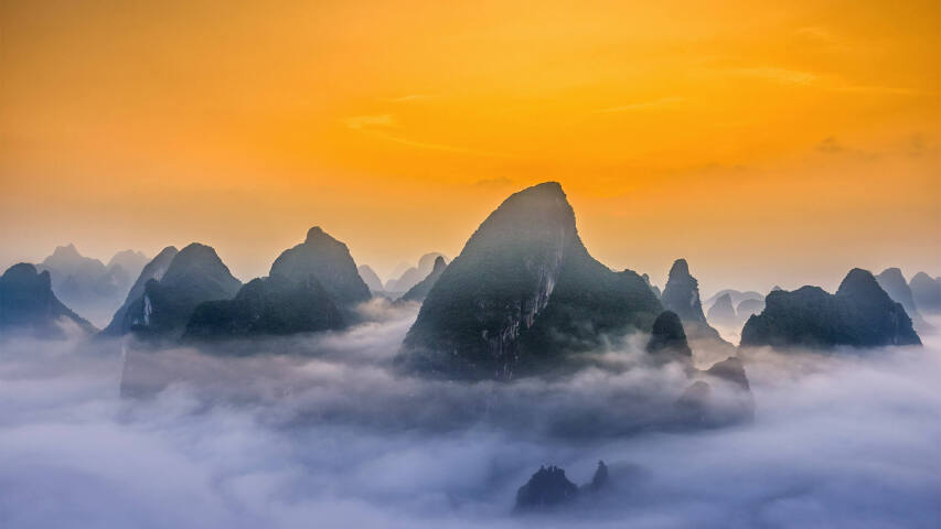日落时分，群山被雾气和云层覆盖，天空为黄色