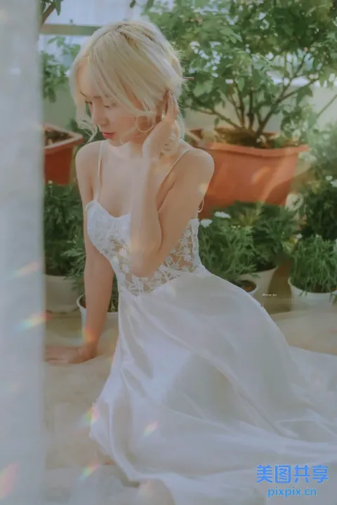 穿着白色连衣裙的金发女人坐在盆栽前的地板上