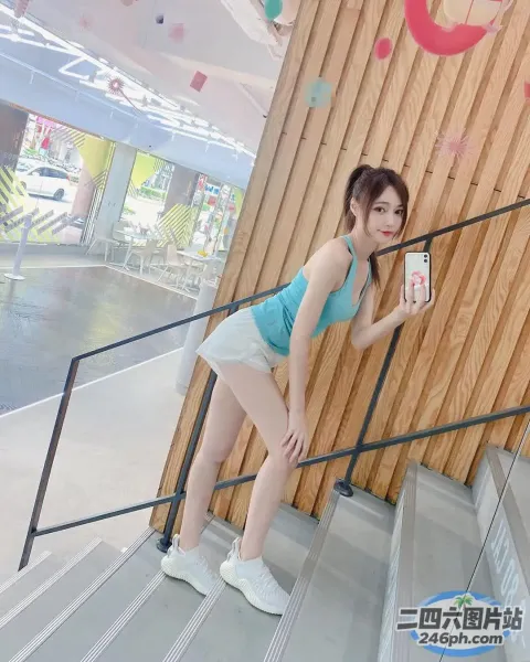 身穿蓝色上衣和白色短裤的女子站在楼梯上，手里拿着手机