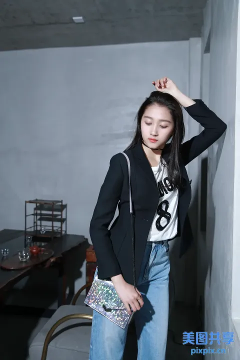 身穿黑色夹克和牛仔裤的女子在房间里拿着钱包摆姿势