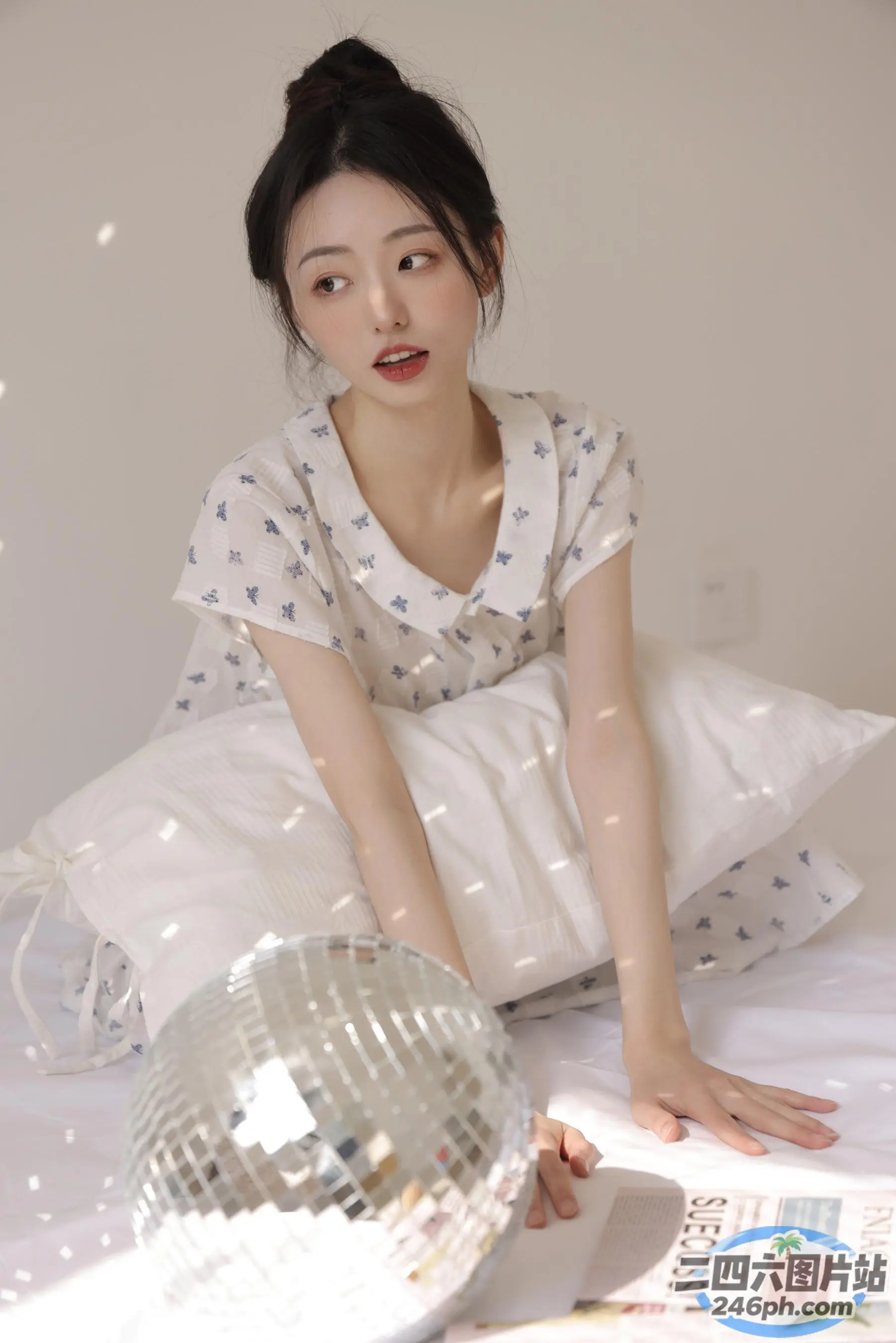有一个女人坐在一张床上，手里拿着一个迪斯科球