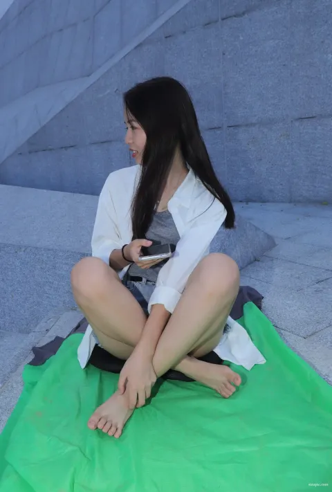 有个女人坐在绿色的毯子上，手里拿着手机