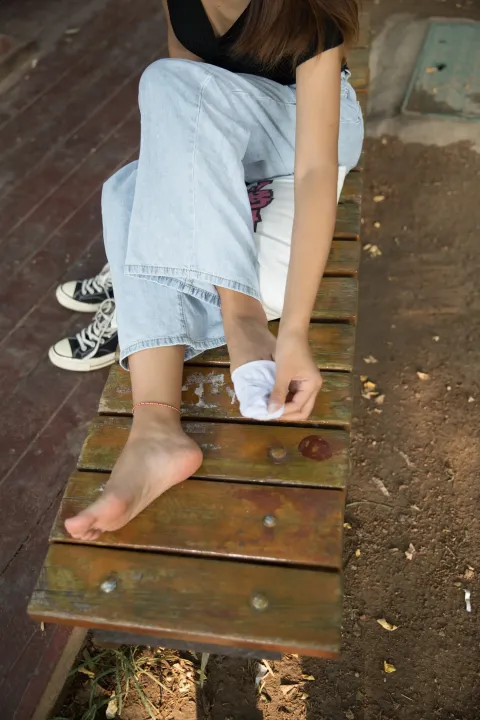 有一个女人坐在长凳上，脚踩在纸上