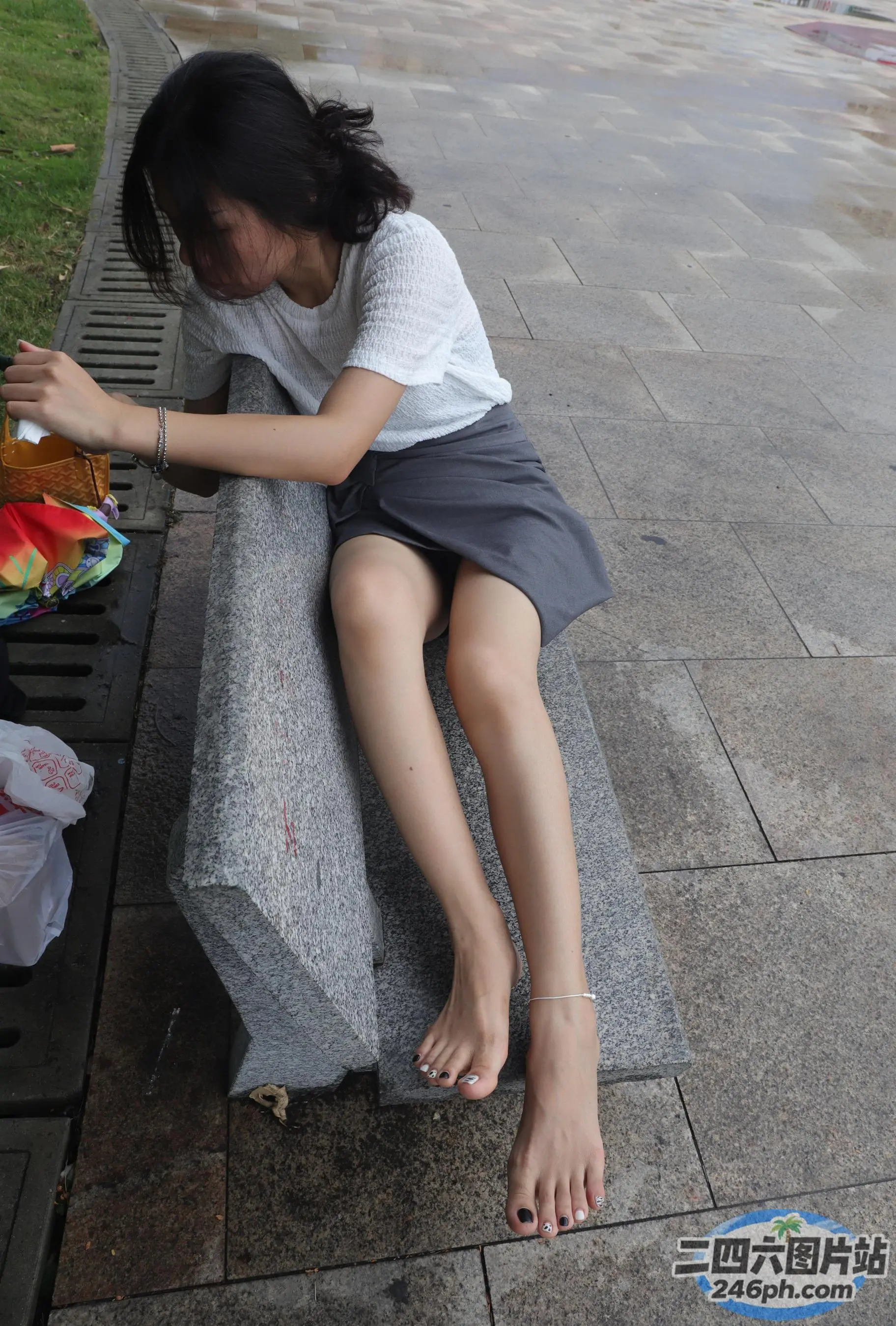有一个年轻女孩坐在长凳上，脚放在一个袋子上