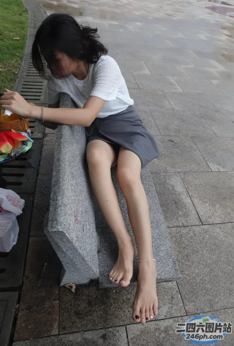 有一个年轻女孩坐在长凳上，脚放在一个袋子上
