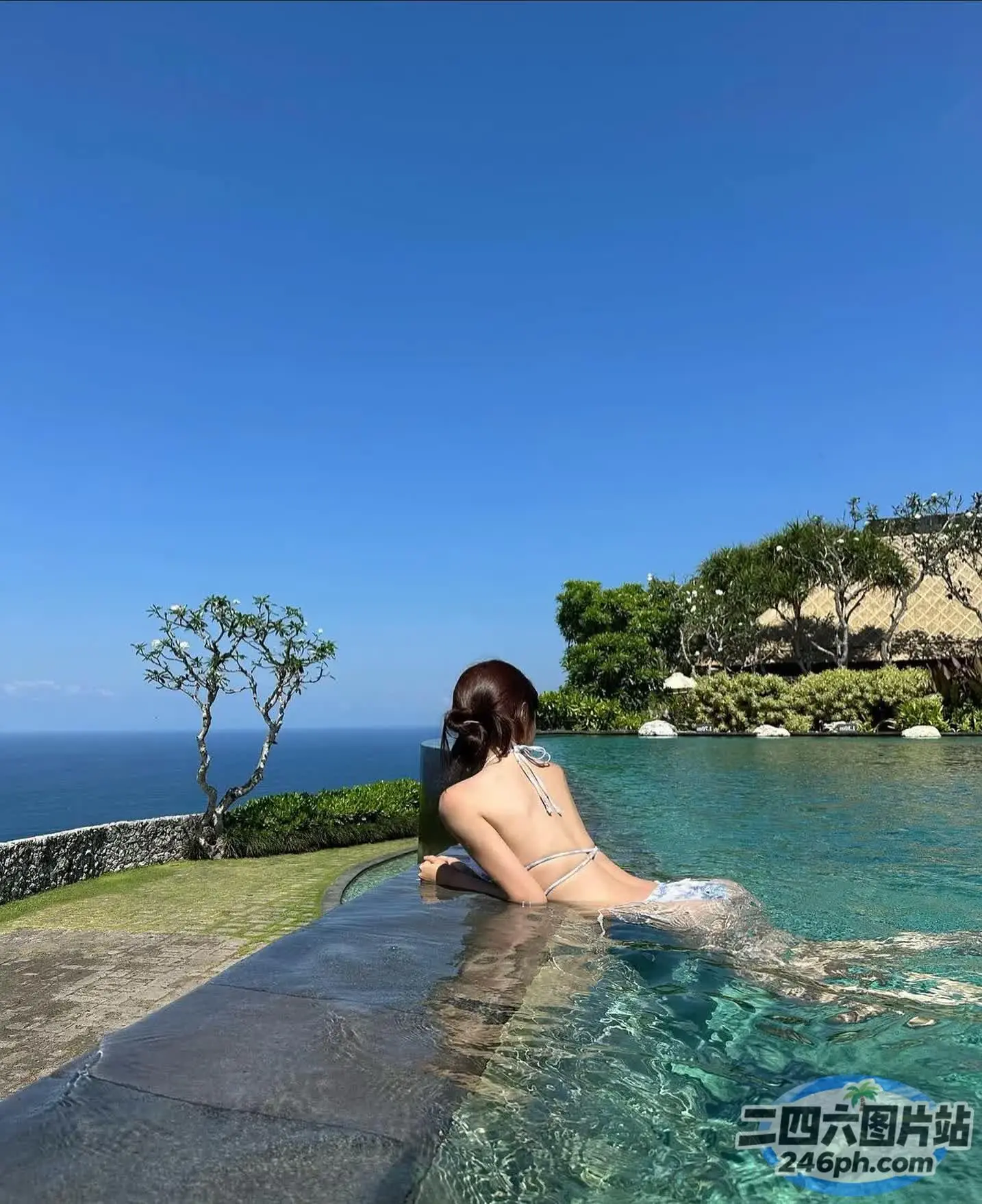 一位穿着比基尼的女人坐在泳池中，可以看到海景