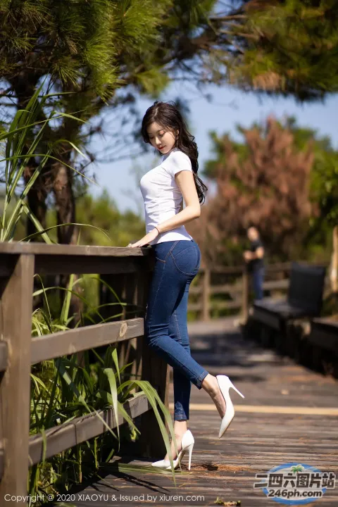 身穿白衬衫和蓝色牛仔裤的亚洲女性靠在木栅栏上