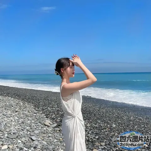 身穿白色连衣裙的女子站在海滩上望向大海