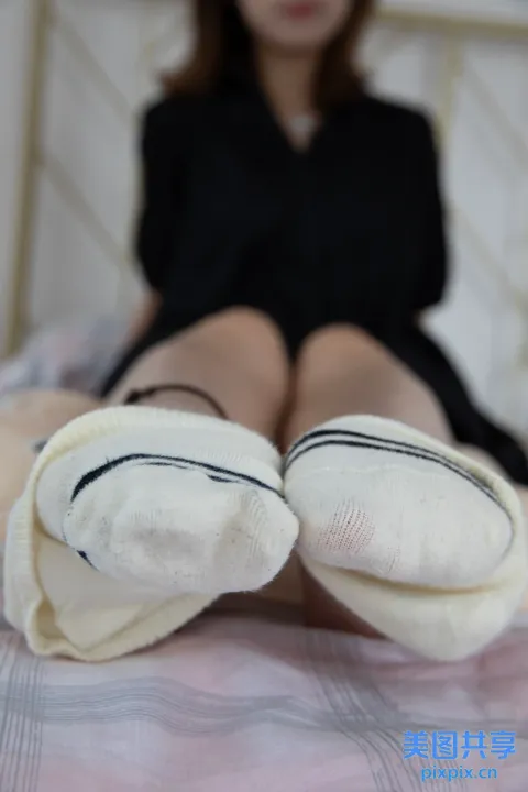 穿着黑色连衣裙的阿拉夫德女人坐在床上，穿着白色袜子